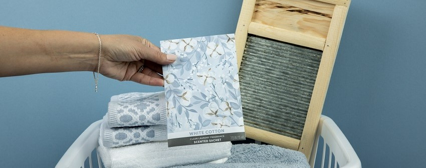 Doftpåse Fresh Scents White Cotton med blommigt mönster, hålls över en tvättkorg med vikta handdukar och en gammaldags tvättbräda – House Of Månsson