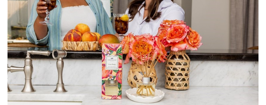 Doftpinnar med doften Coco Peach från Greenleaf hos House Of Månsson placerade på köksbänk tillsammans med persikor, dekorativa blommor, doftdiffuser och stilren heminredning i ljust kök